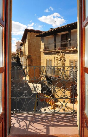 A view through a wrought iron gate into a narrow street with buildings featuring traditional architecture and balconies. - Casona del Boticario (San Vicente de la Sonsierra)