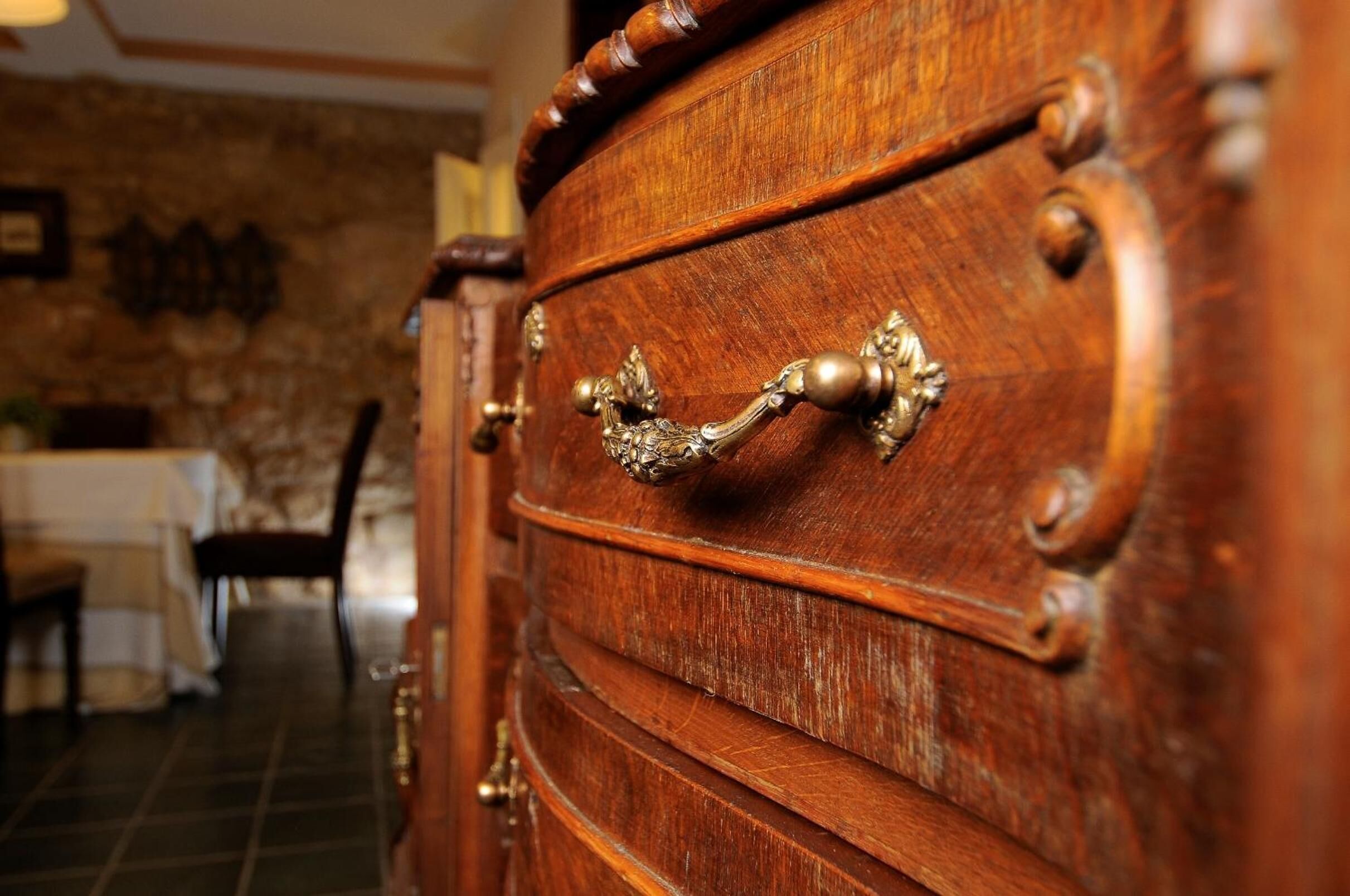 A wooden cabinet with ornate brass handles and a stone wall in the background.