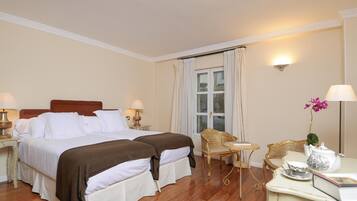 A hotel room with two beds, a sitting area with a table and chairs, a window with curtains, and a vase with flowers.