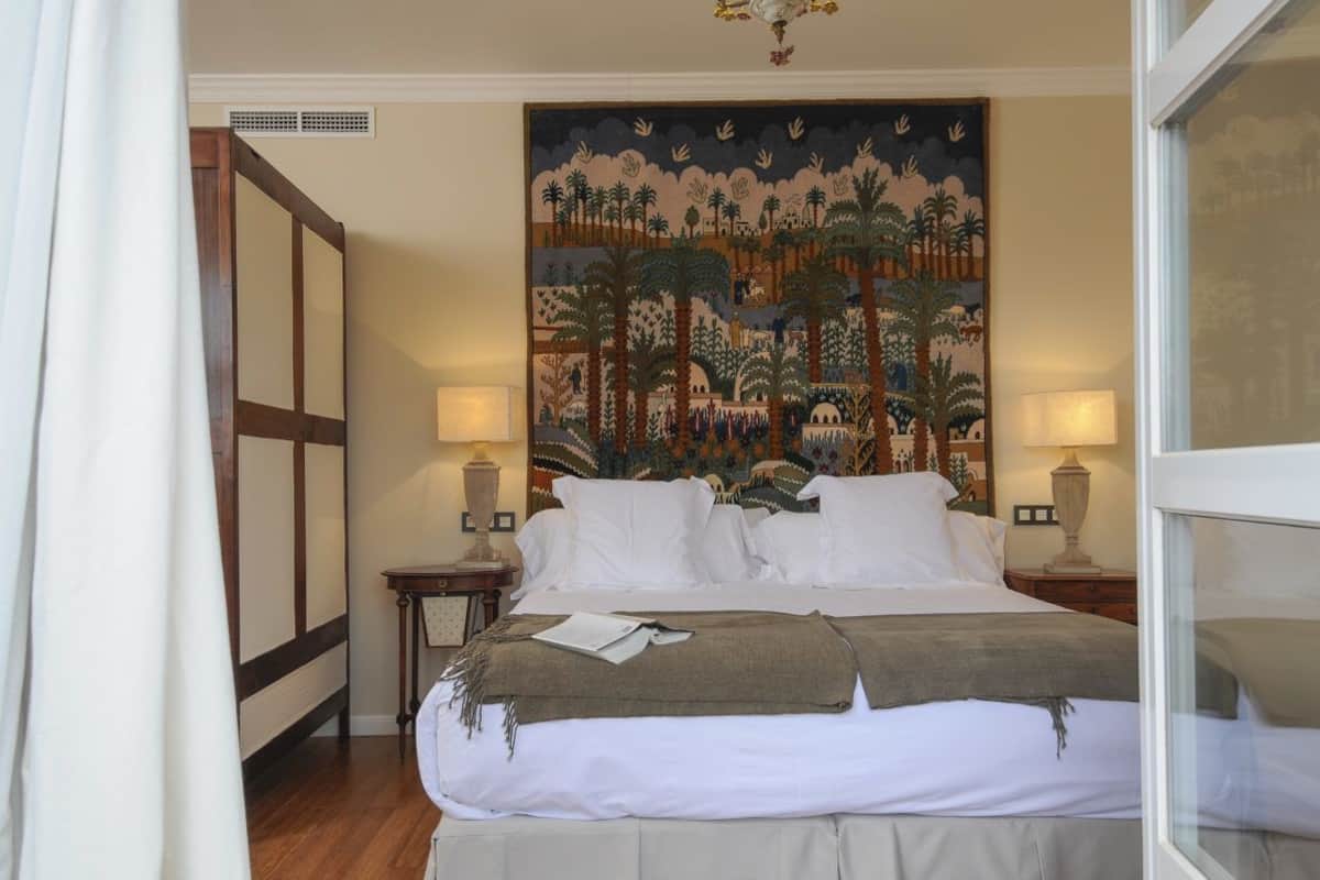 Une chambre d’hôtel avec un grand lit, deux tables de chevet avec des lampes, une tapisserie au mur et un plancher en bois.