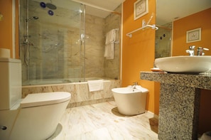 A bathroom with a toilet, a bidet, a bathtub, and a glass-enclosed shower area. - Casona del Boticario (San Vicente de la Sonsierra)