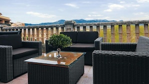 A rooftop terrace with wicker furniture, a glass-top table, and a potted plant.