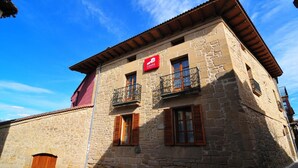 A stone building with a red sign, wooden shutters, and a balcony.
