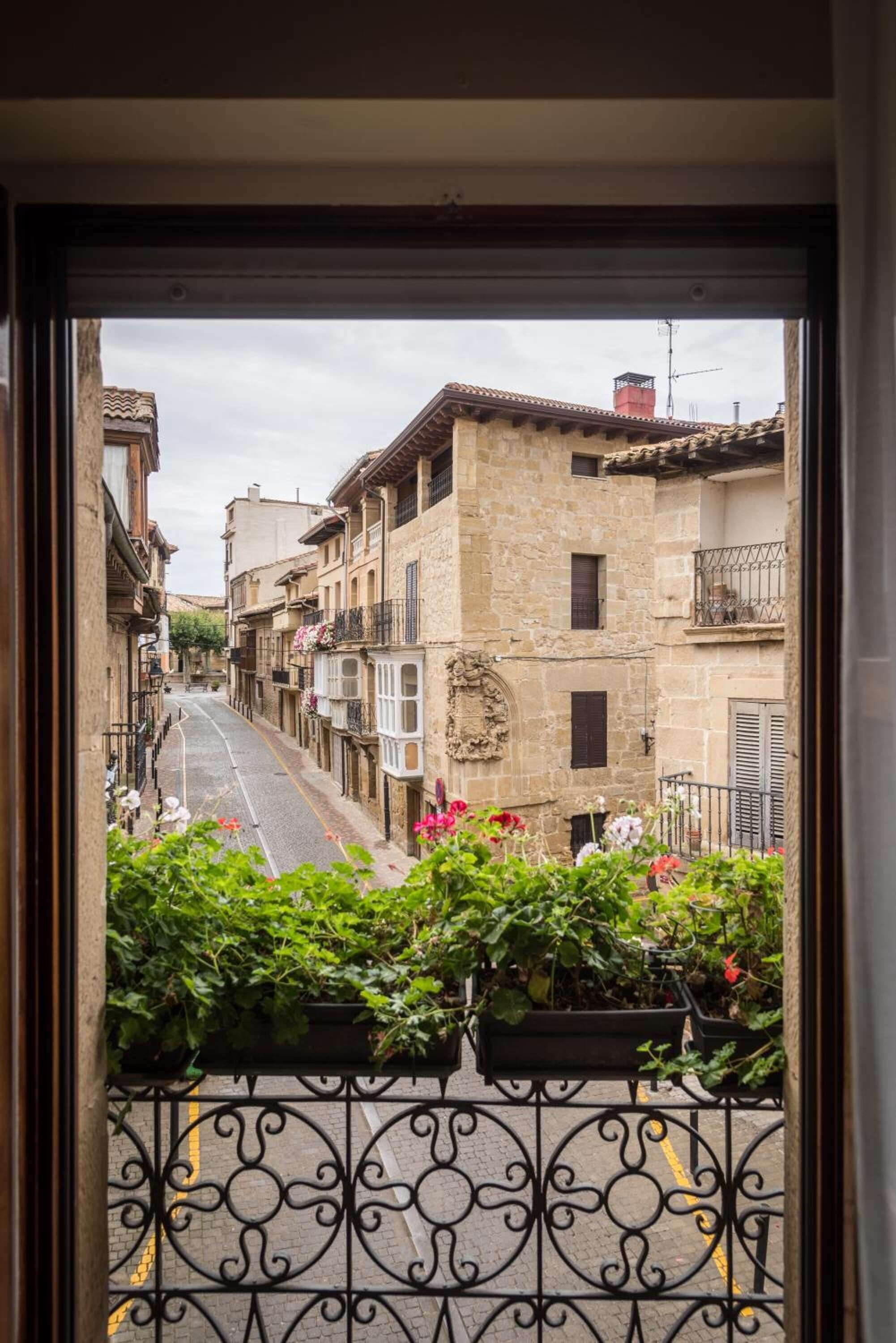 A narrow street with stone buildings, a wrought iron fence, and potted plants.