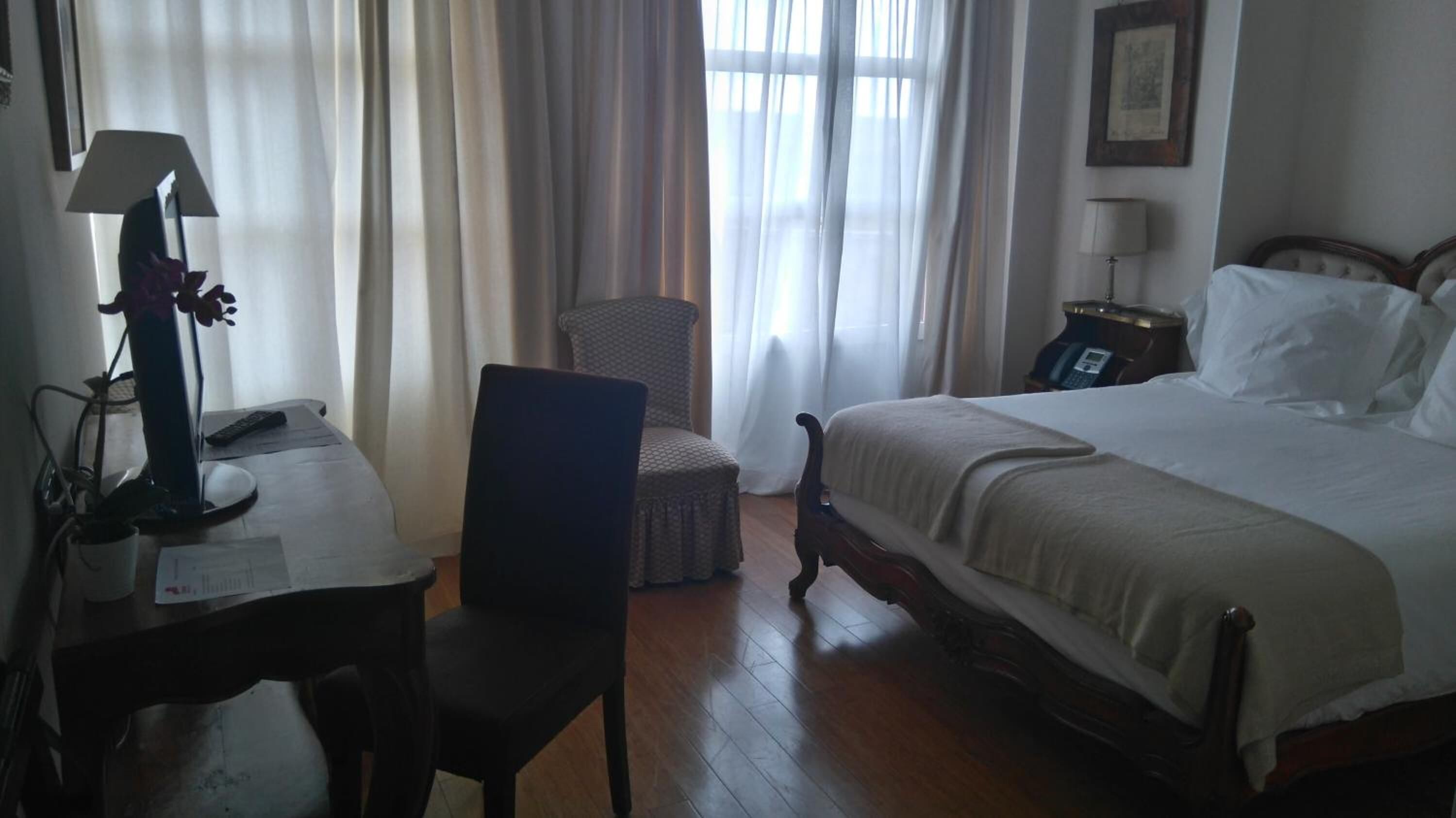 Una habitación de hotel con una cama, un escritorio con lámpara, una silla y una mesita de noche con teléfono.