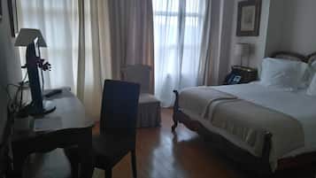 Una habitación de hotel con una cama, un escritorio con lámpara, una silla y una mesita de noche con teléfono.