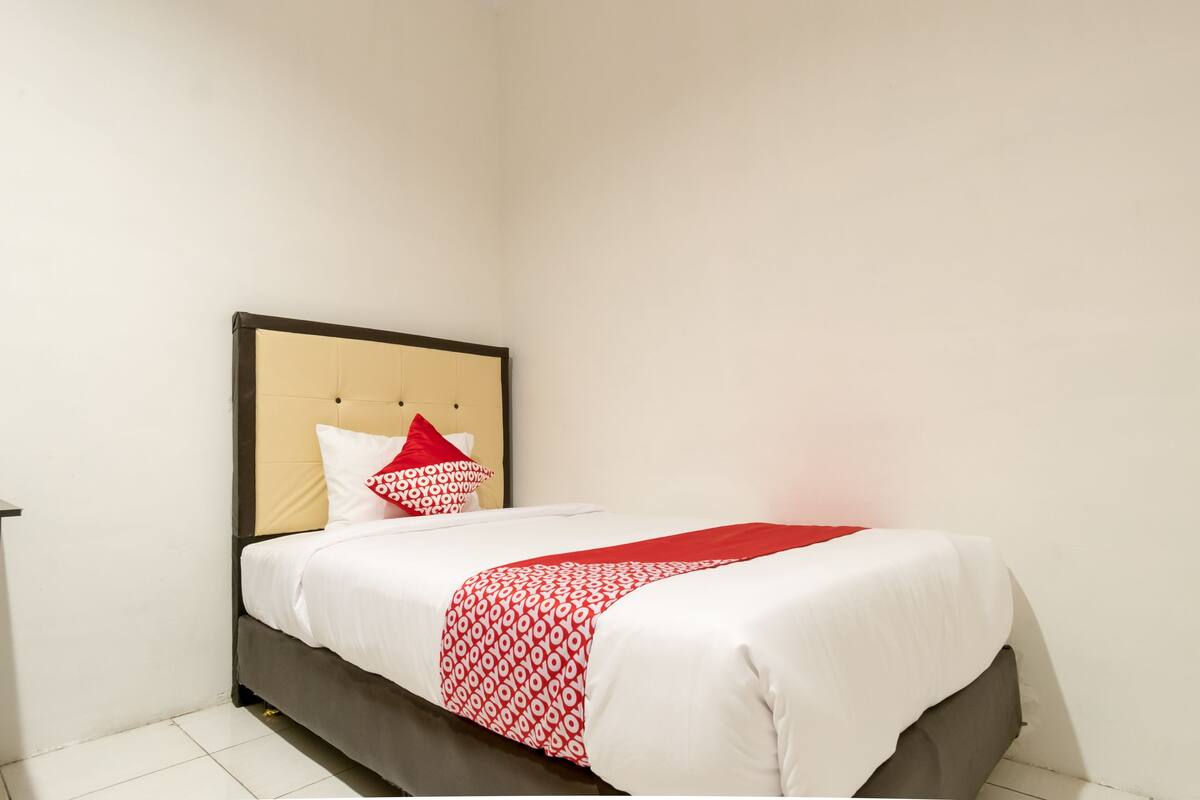 A neatly made bed with a patterned bedspread and pillows, a headboard, and a plain white wall.
