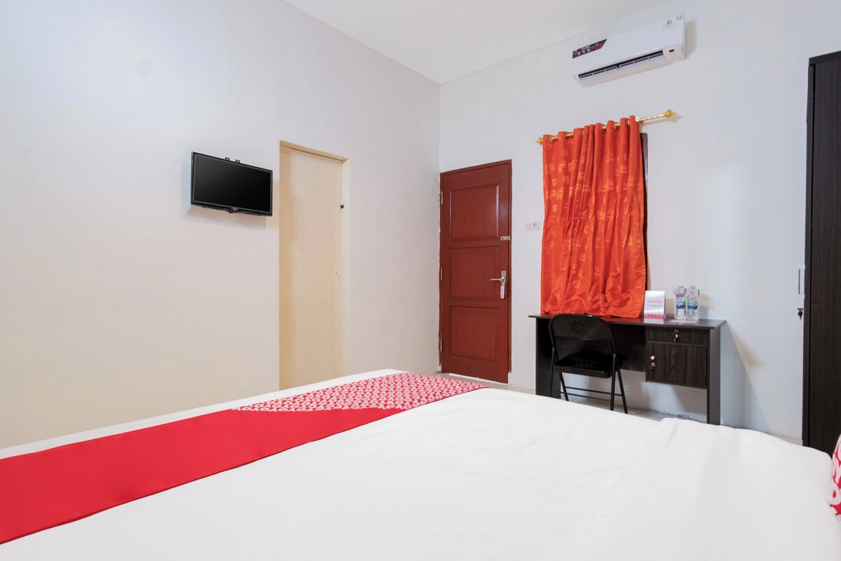 Quarto de hotel com cama, escrivaninha, cadeira, ar condicionado e televisão.