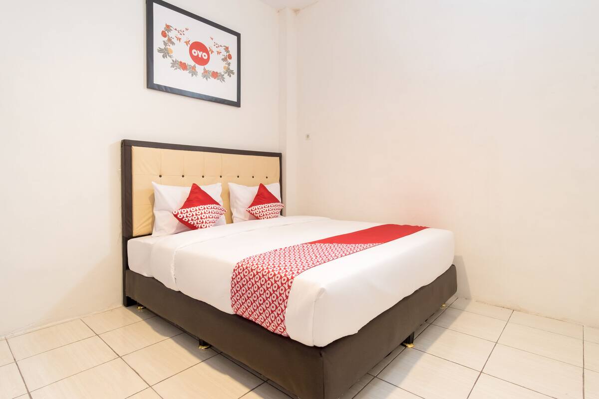 A neatly made bed with a patterned bedspread and pillows, a framed picture on the wall, and a tiled floor.