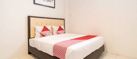 A neatly made bed with a patterned bedspread and pillows, a framed picture on the wall, and a tiled floor.