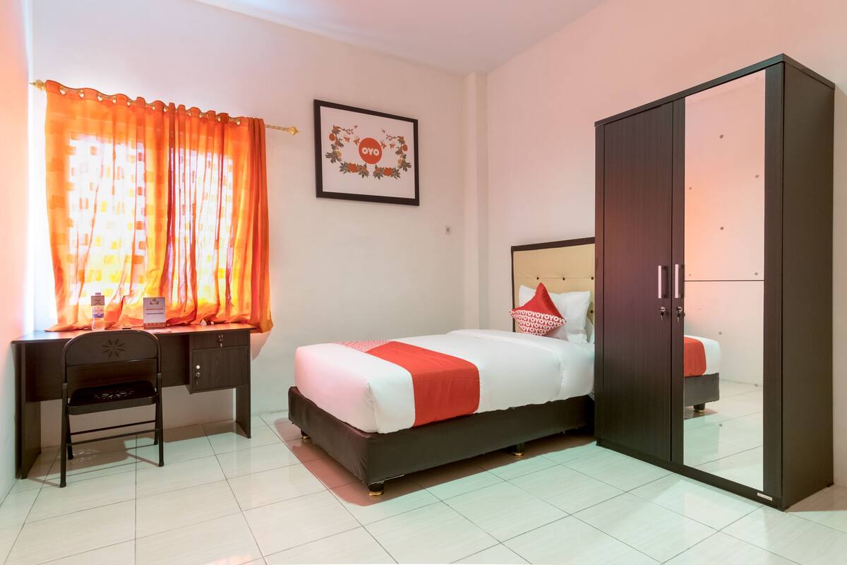 A bedroom with a bed, a desk, a chair, a wardrobe, and a framed picture on the wall.