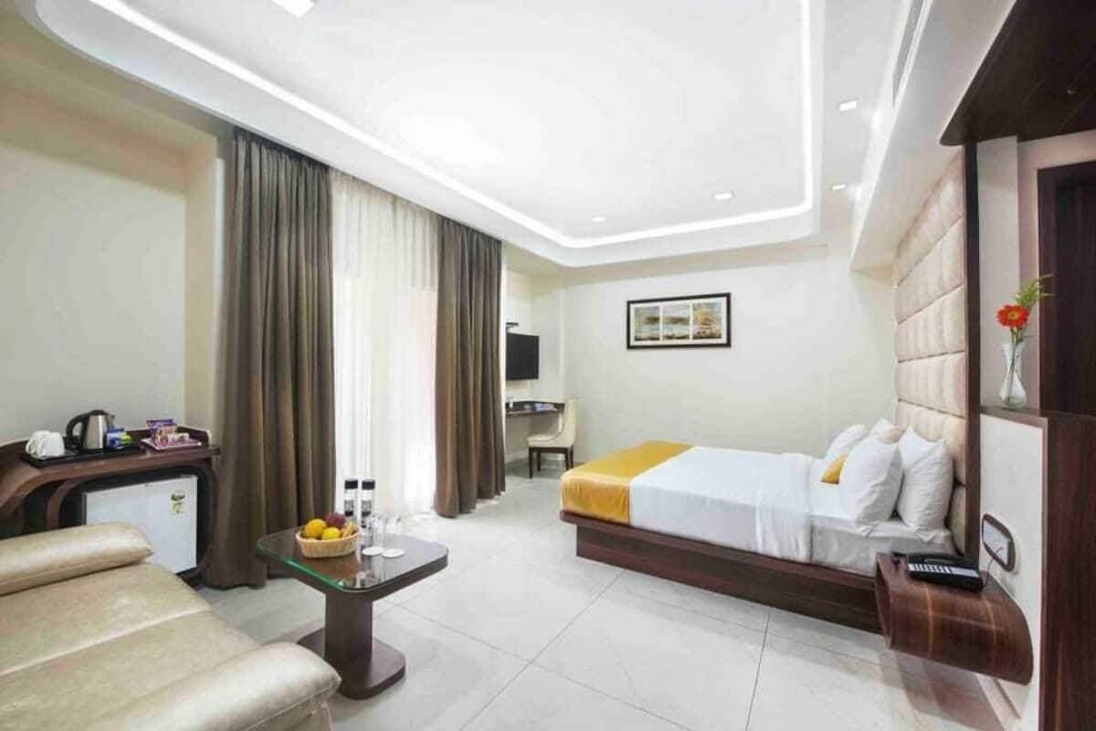 A hotel room with a bed, a desk, a chair, a small table with a fruit bowl, and a TV.