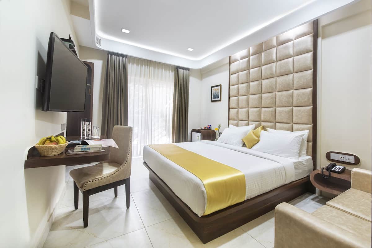 A hotel room with a bed, a desk with a television, a chair, and a bedside table with a phone.