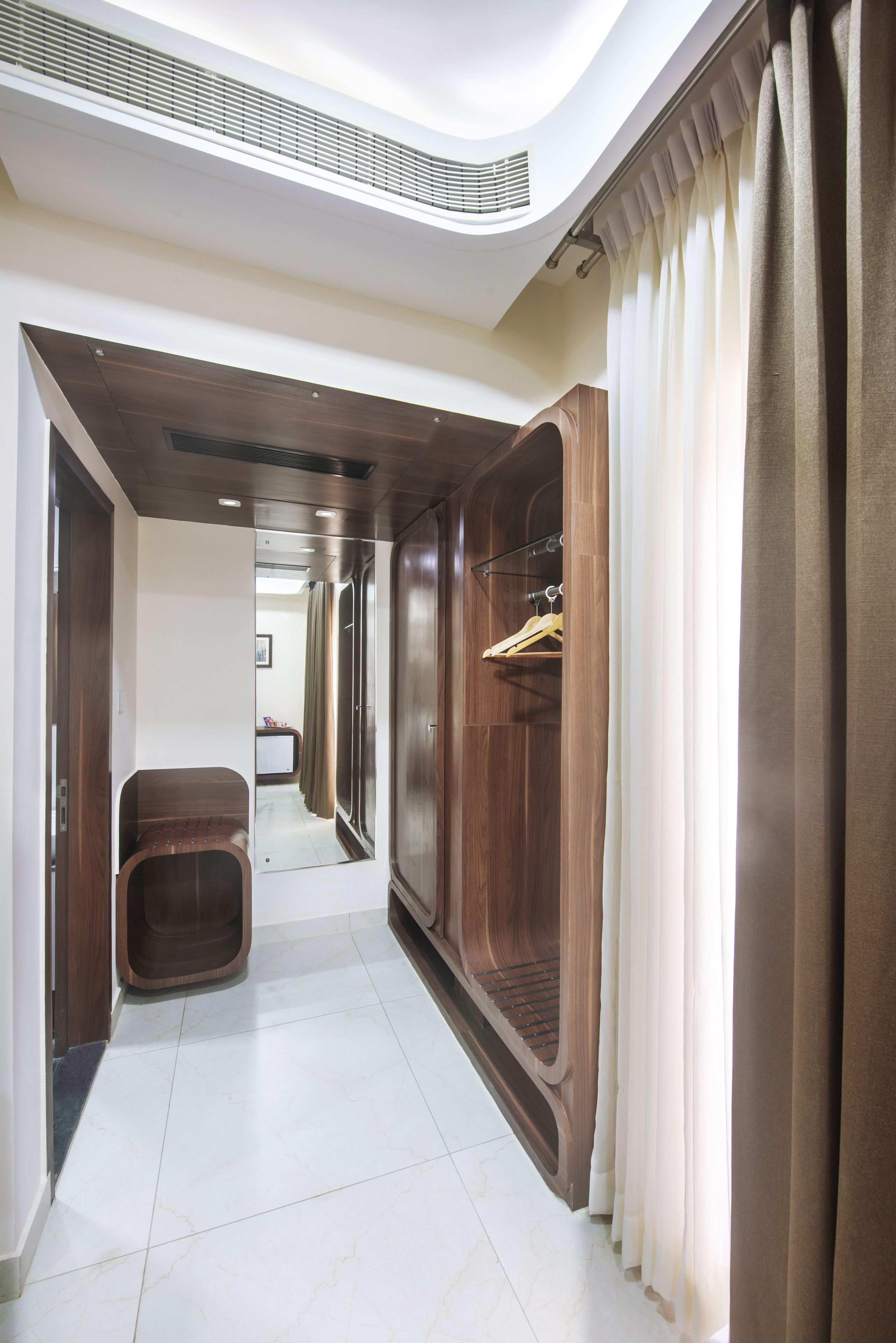 A hallway with wooden paneling, a bench, and a mirror reflecting a room with curtains.