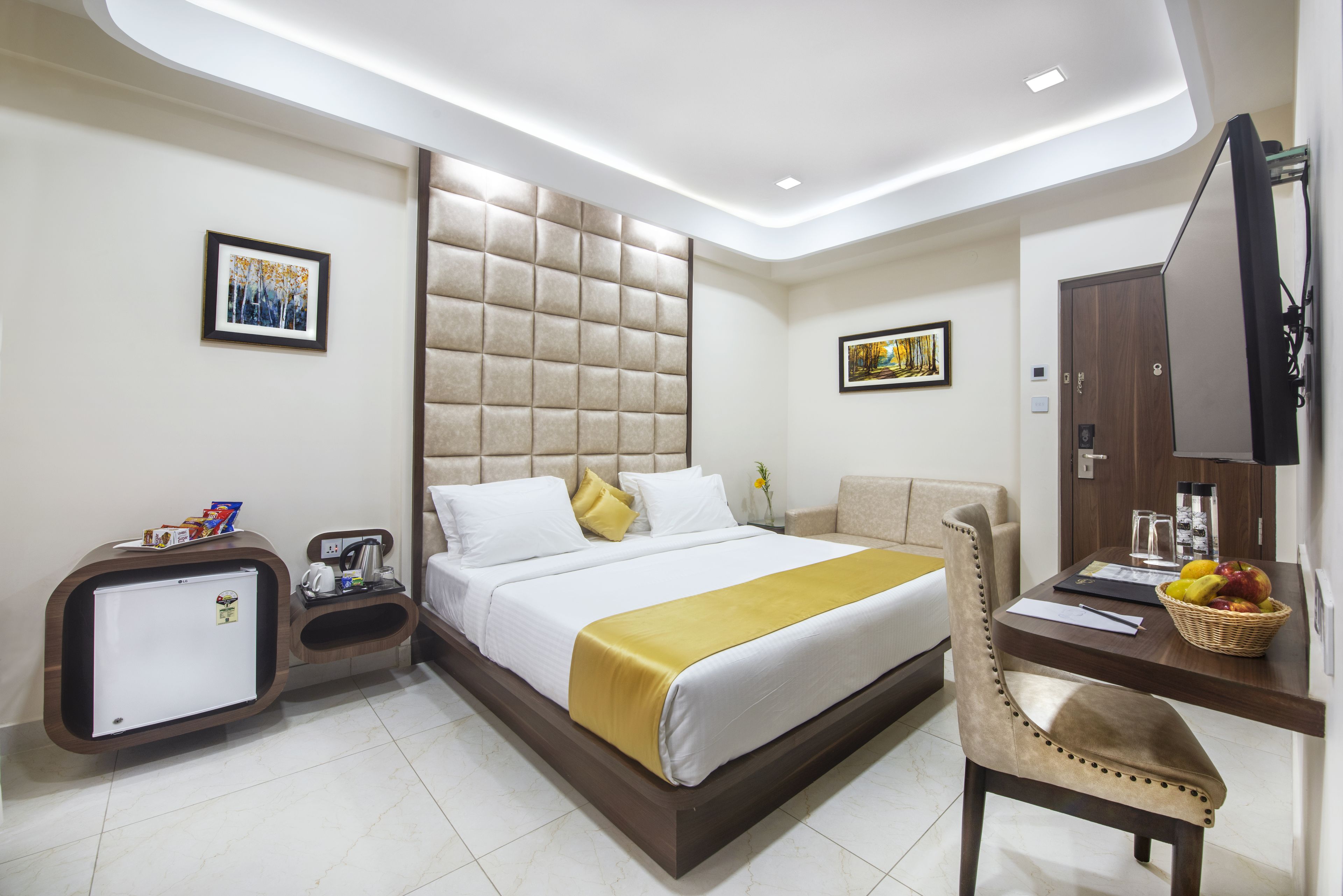 A hotel room with a bed, a desk, a chair, a television, and a minibar.