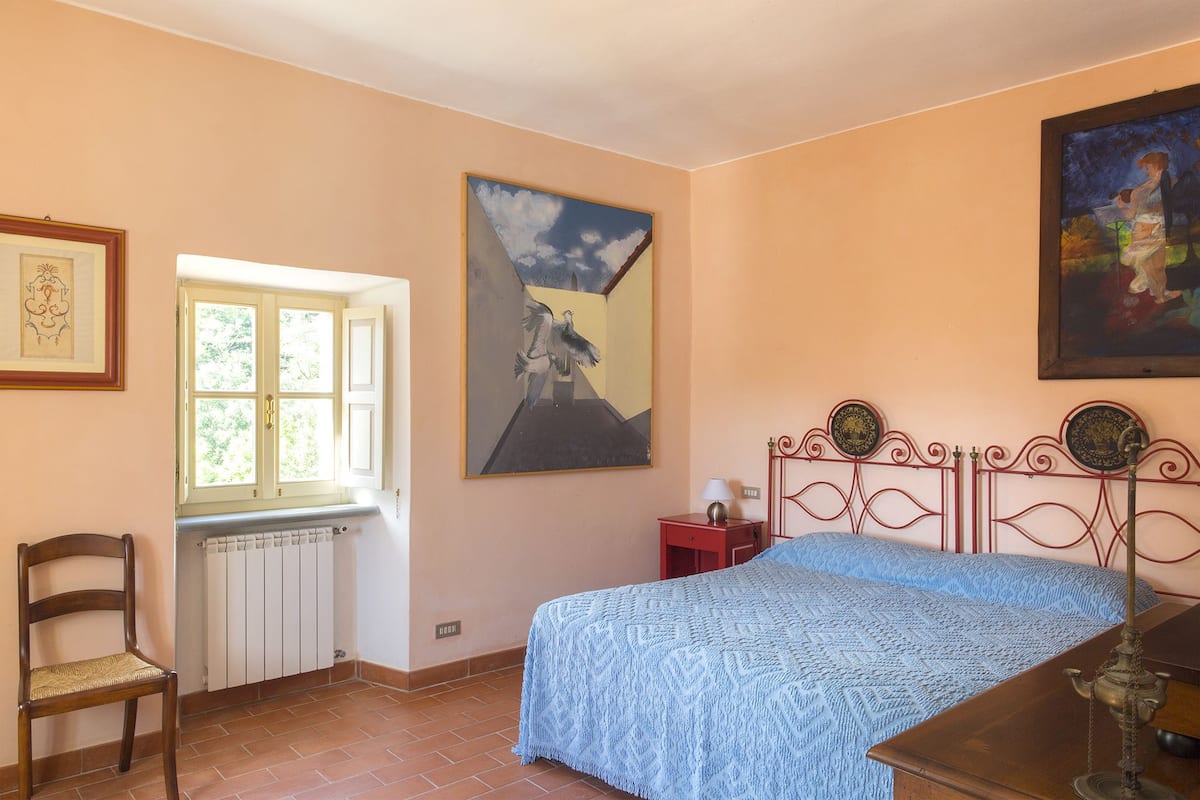 Ein Schlafzimmer mit Bett, Stuhl, Heizkörper, Fenster und Bildern an den Wänden.