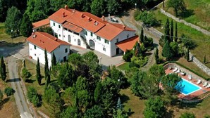 Une grande maison blanche à deux étages, avec un toit rouge, entourée d’une végétation luxuriante et dotée d’une piscine.