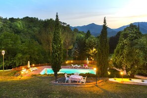 Un espace piscine aménagé avec des chaises longues et une table, entouré d’arbres et d’une clôture en bois.