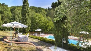 Un jardin avec une piscine, une terrasse dotée de mobilier d’extérieur et un chemin en briques.
