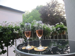 Two glasses of wine on a glass table outdoors with greenery in the background.