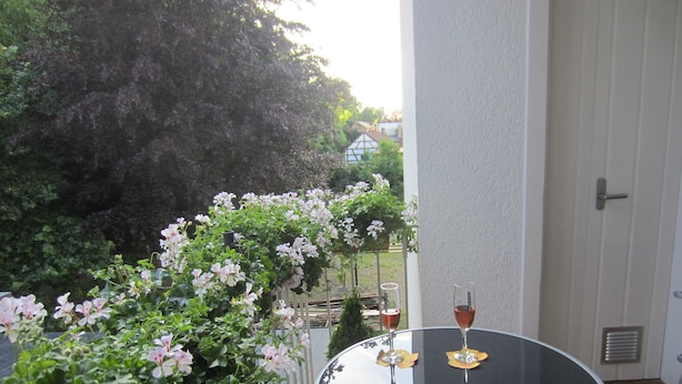 Uma mesa redonda com duas taças de vinho numa varanda com vista para um jardim e uma porta branca.