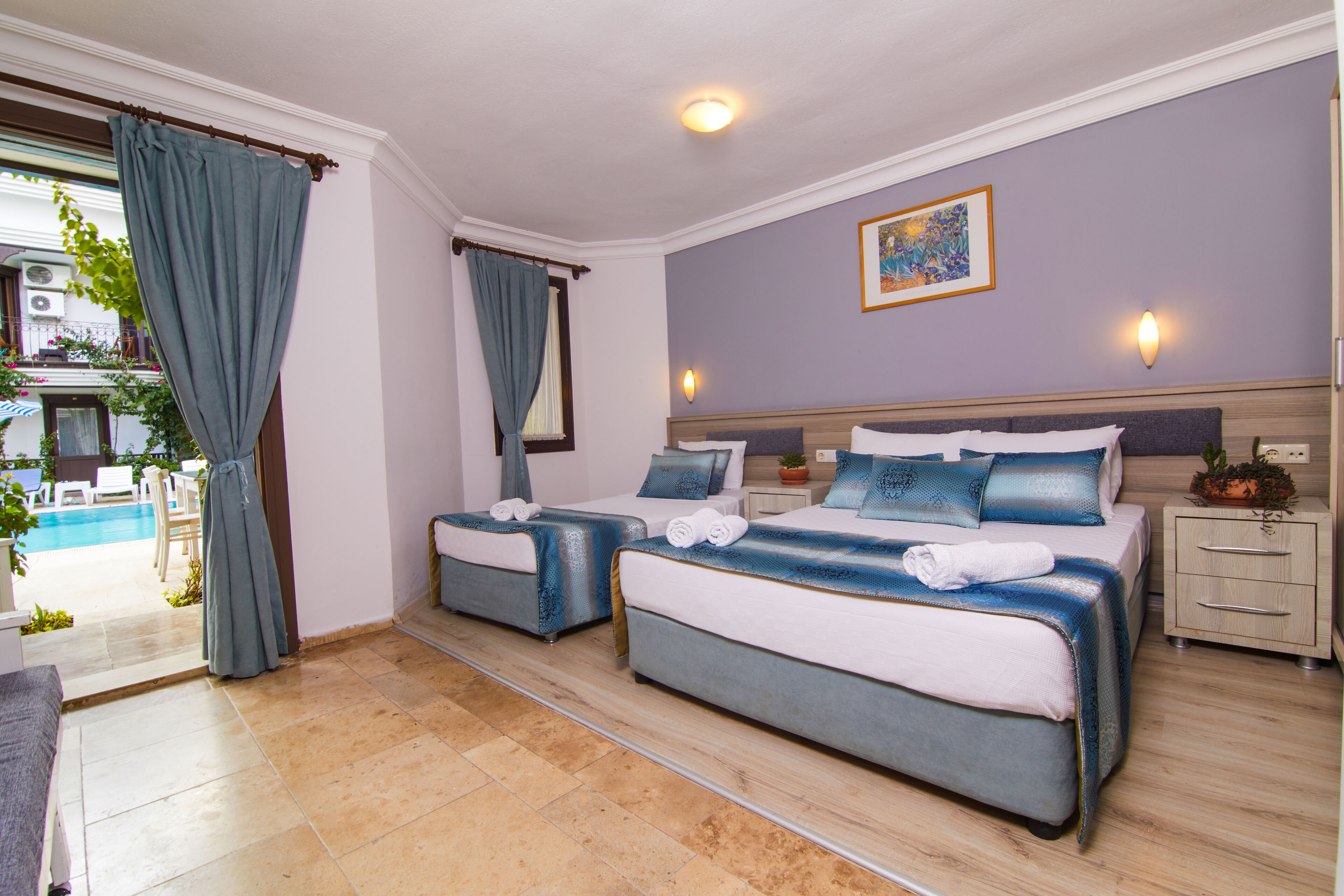 A hotel room with two beds, a small bedside table, a nightstand, a window with curtains, and a view of the pool area.