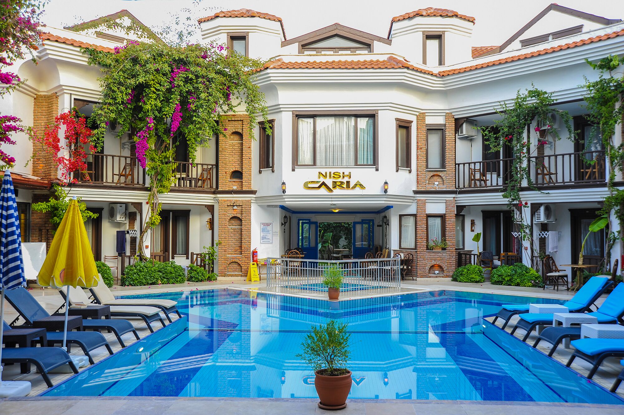 A hotel with a pool, outdoor seating, and a sign reading "NISH CARIA".