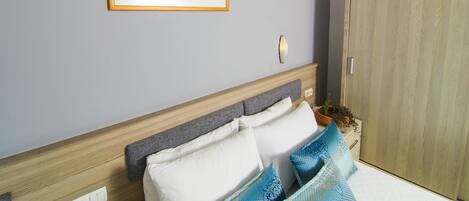 Un dormitorio con cama, cabecera, lámpara de pared, cuadro enmarcado y puerta de madera.