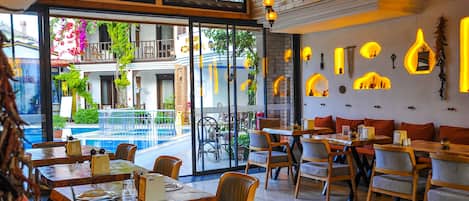 A restaurant with indoor seating, a pool view, and a wooden ceiling.