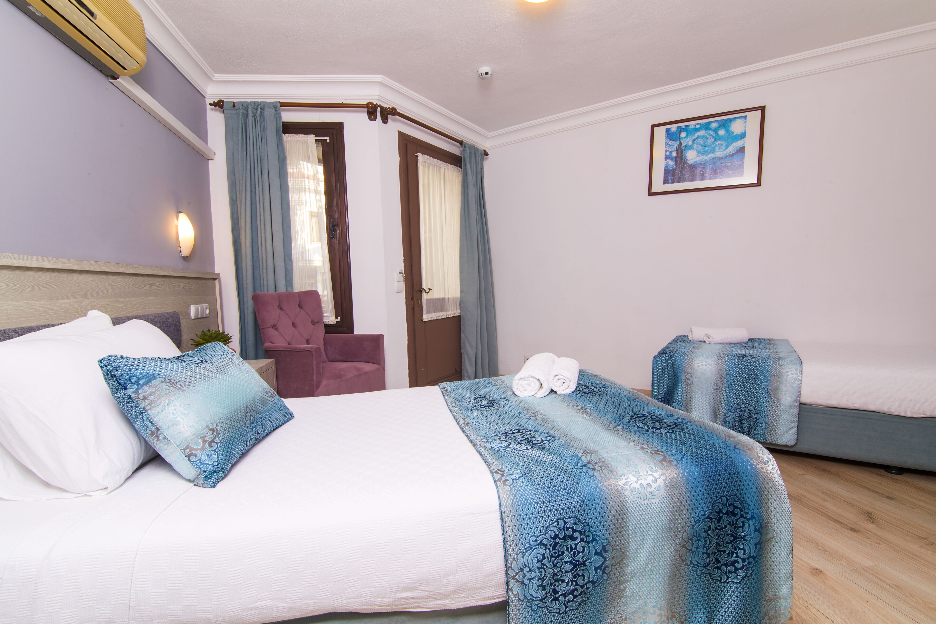 A hotel room with a bed, a chair, a small table, and a painting on the wall.