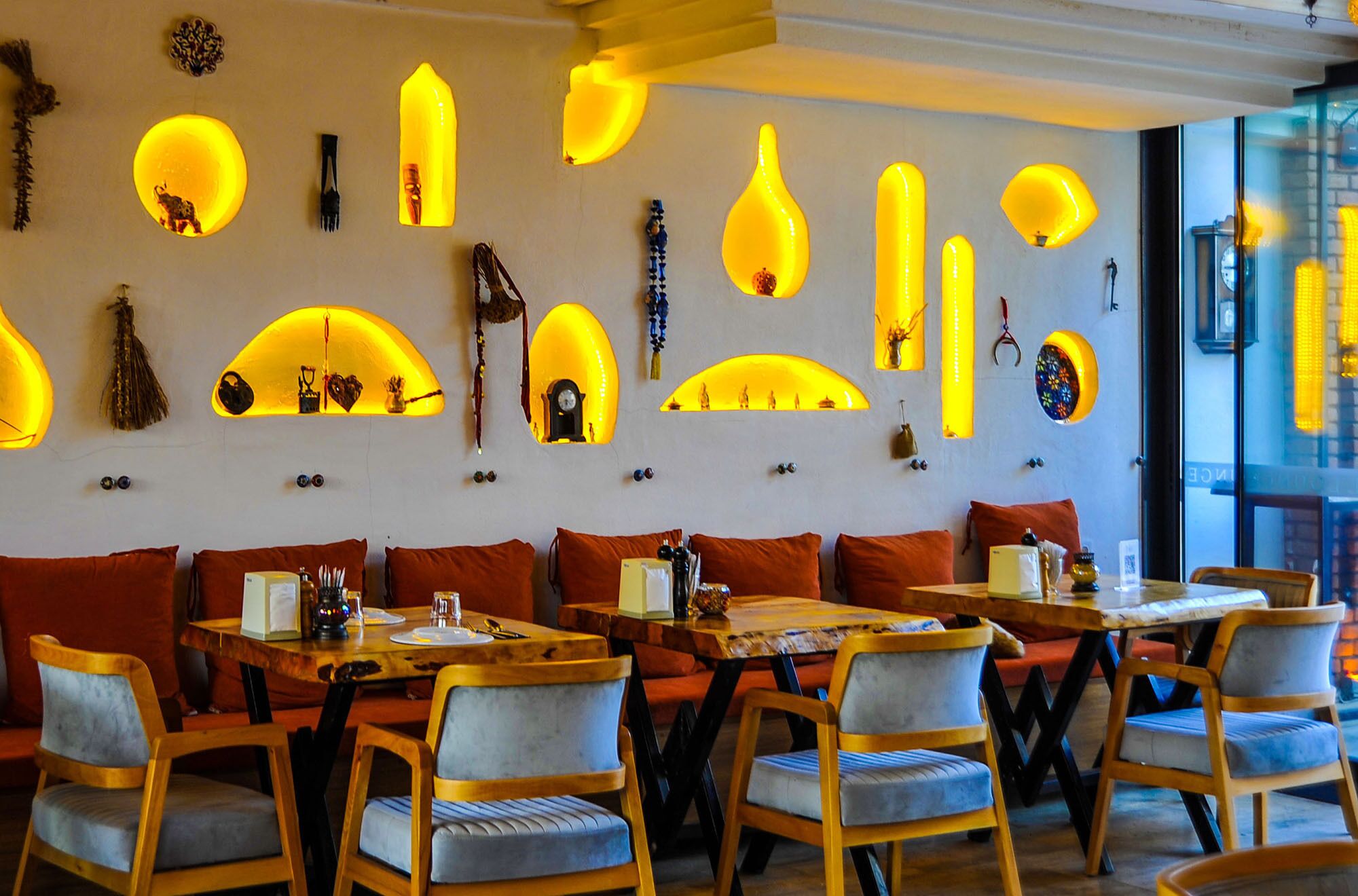 A restaurant with tables and chairs, a wall with illuminated shapes, and a view of the street outside.