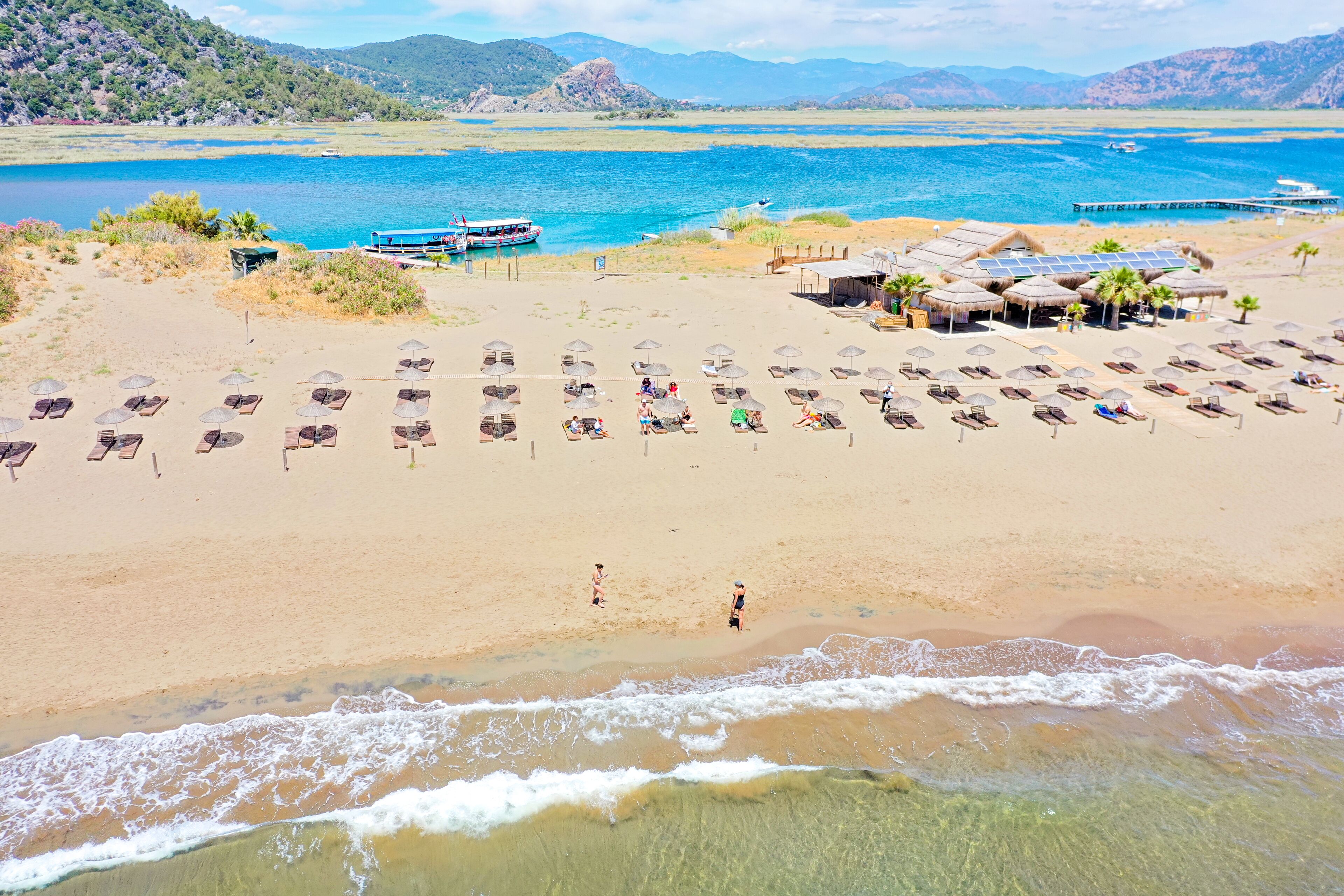 Una playa con filas de tumbonas y sombrillas, un bote en el agua y un muelle al fondo.