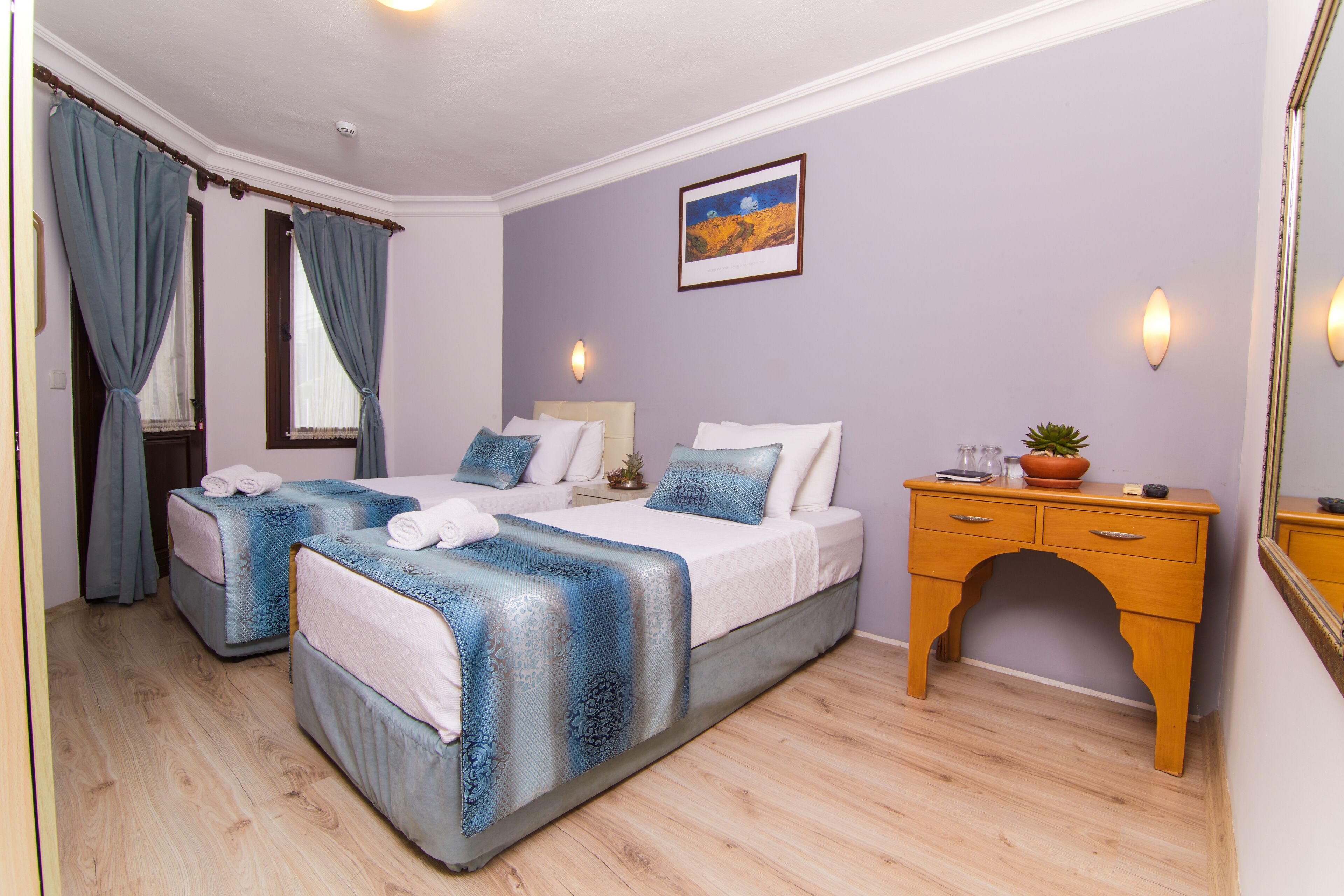 A hotel room with two beds, a wooden dresser, a nightstand, and a painting on the wall.