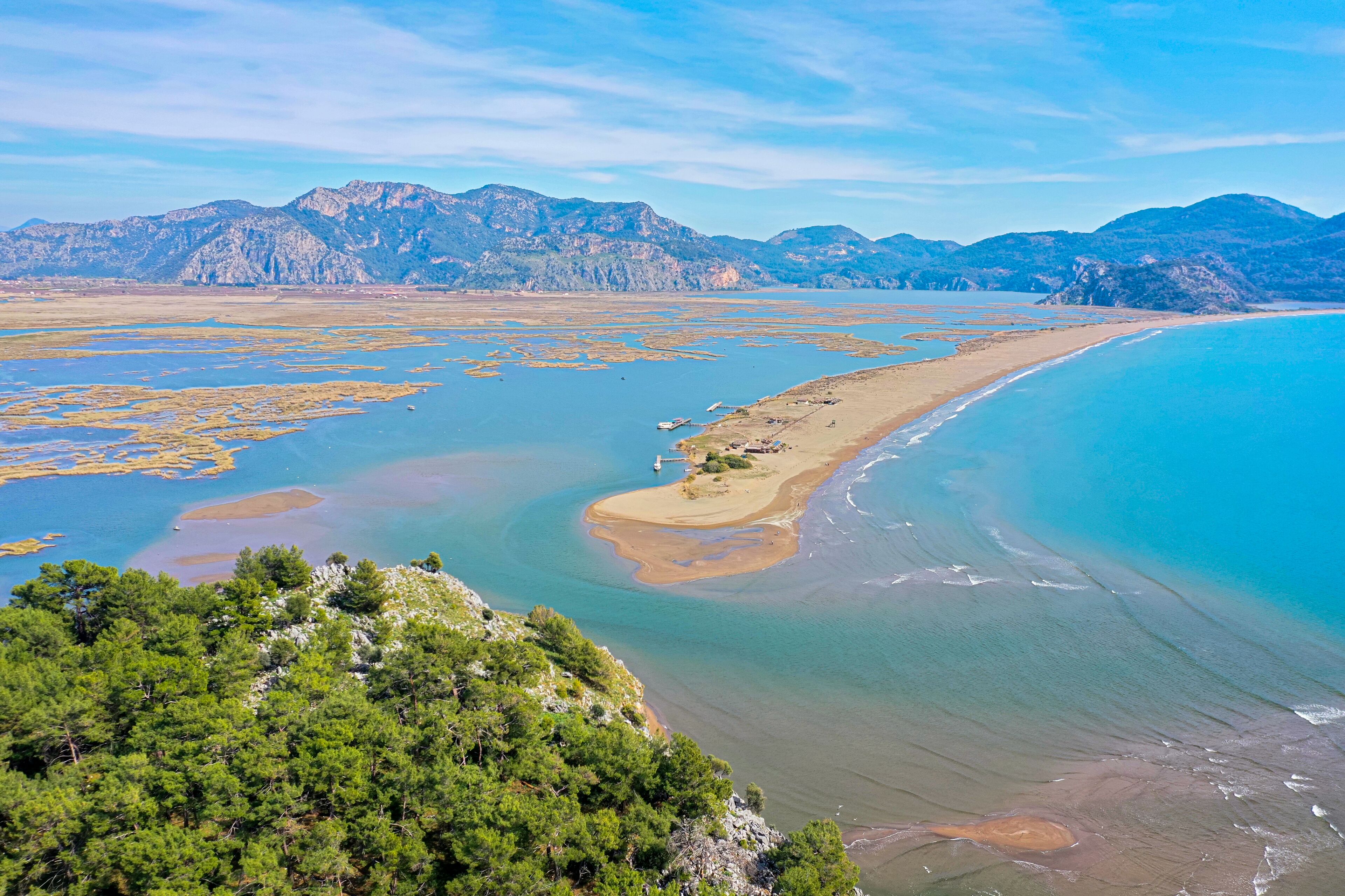 A coastal landscape with a beach, clear waters, and mountains in the background.