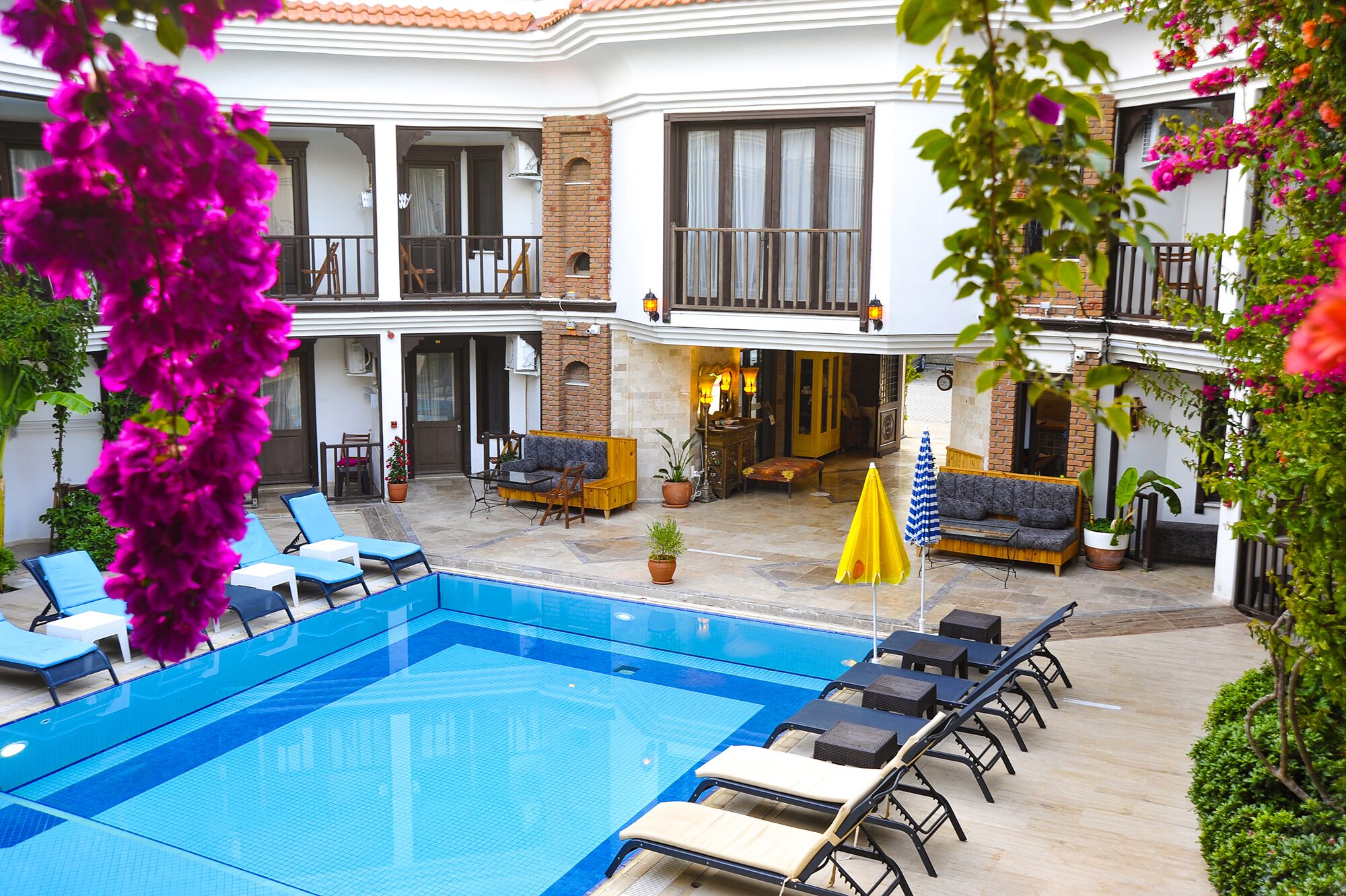 A swimming pool with lounge chairs and a seating area with a yellow umbrella.