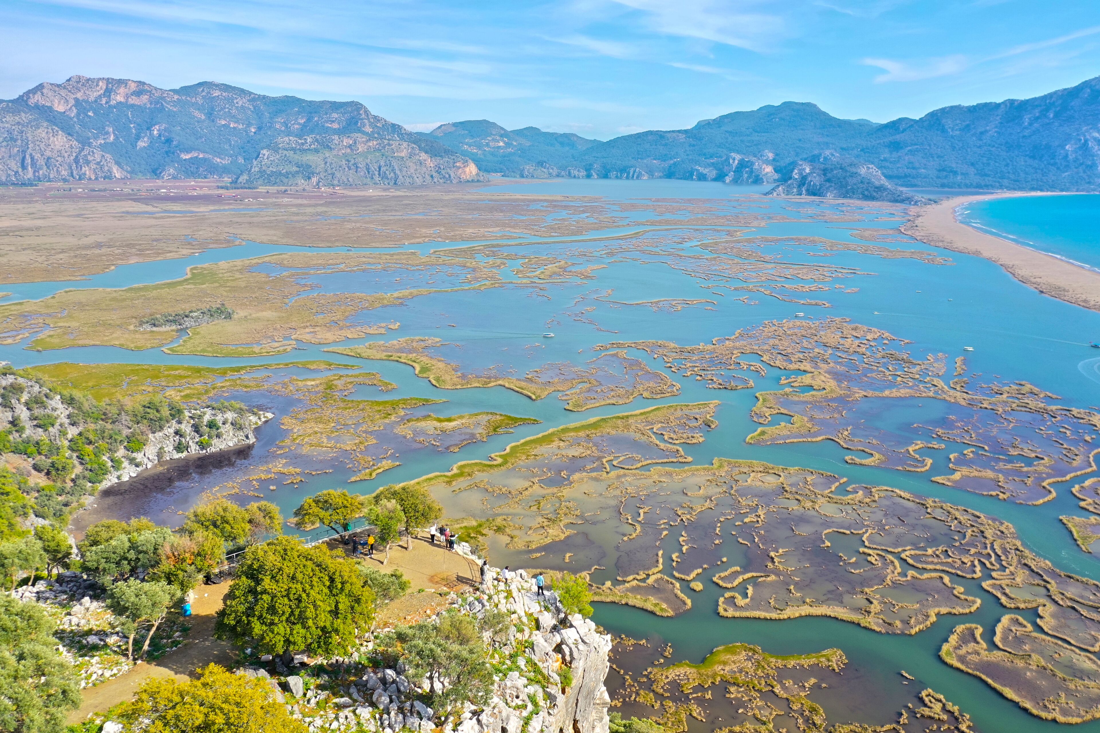 A coastal landscape with a rocky shoreline, a bay with clear water, and a mountainous backdrop.
