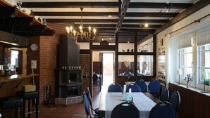 A restaurant with a brick fireplace, wooden beams, and a long table with chairs.