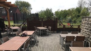 An outdoor patio area with wooden tables and chairs, a stone floor, and a wooden fence.