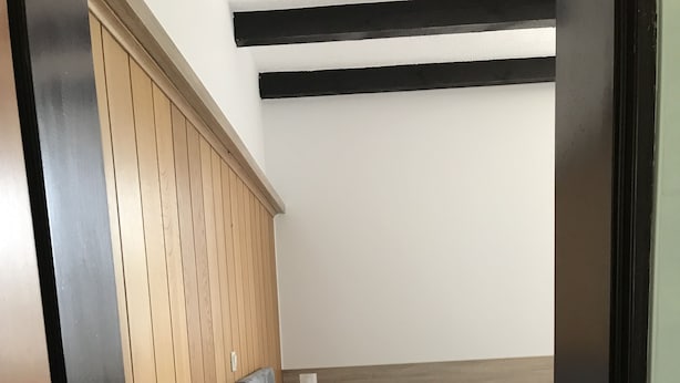 A bedroom with a wooden headboard, a bedside table with a lamp, a bed with white linens, and a view of the ceiling.