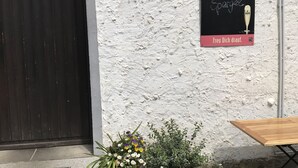 A building entrance with a black door, a signboard advertising 'Frischer Spargel', and two flower arrangements on the steps.