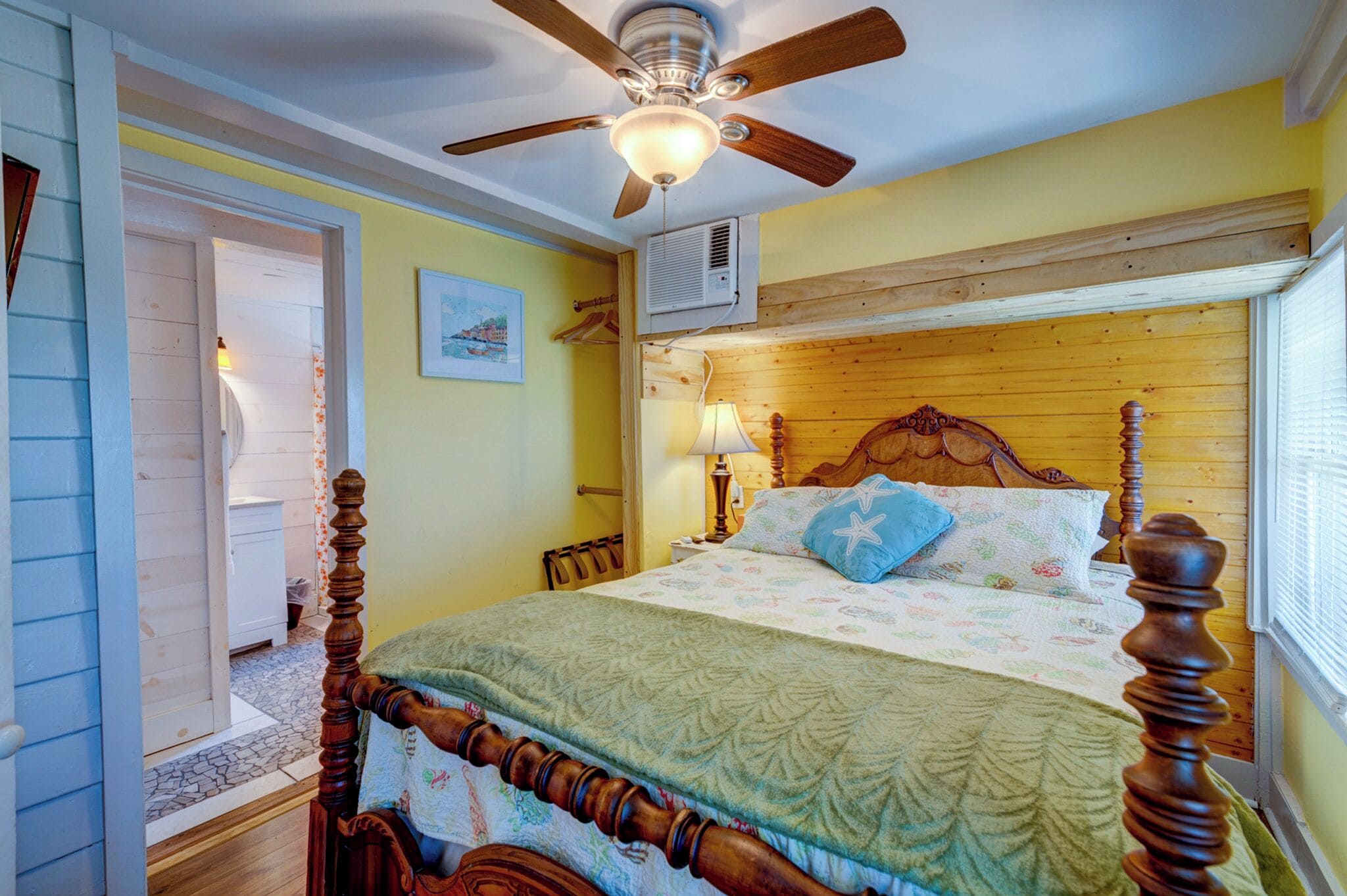 A bedroom with a wooden bed, a ceiling fan, a nightstand, and a window with blinds.