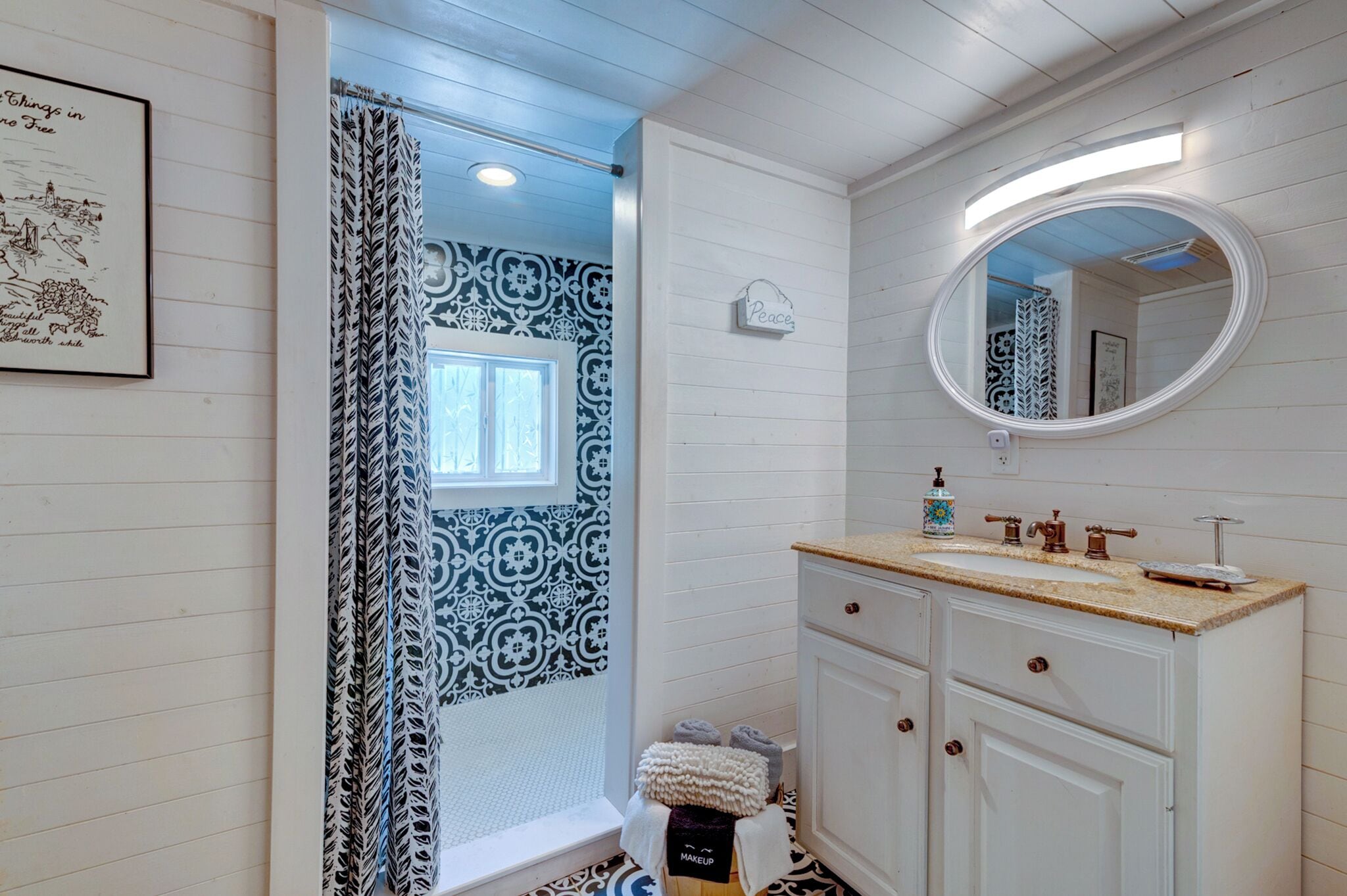 A bathroom with a white vanity, a round mirror, a patterned shower curtain, and a framed picture on the wall.