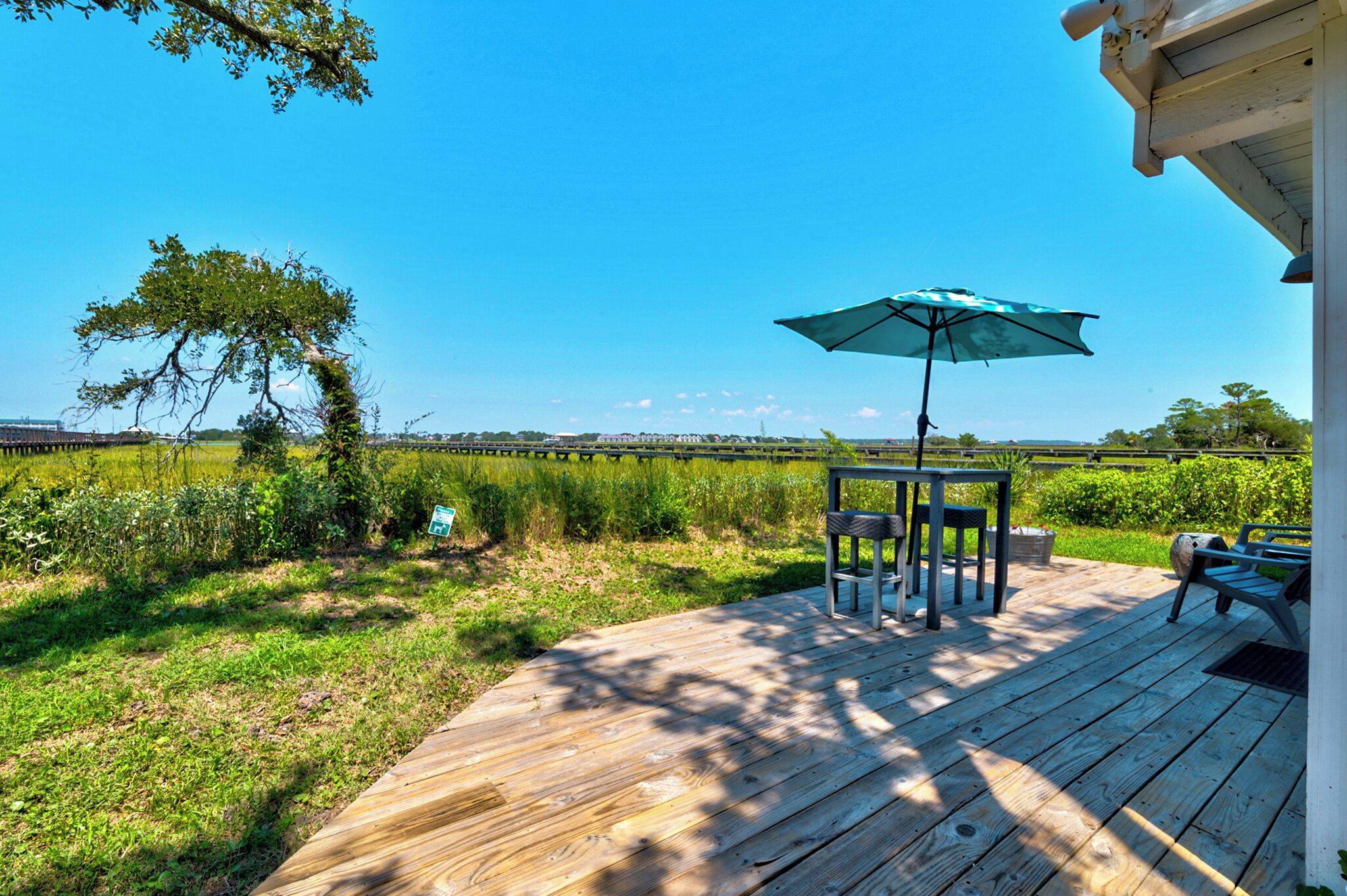 Une terrasse en bois avec une table et des chaises, un parasol et une vue sur un champ et des bâtiments éloignés.