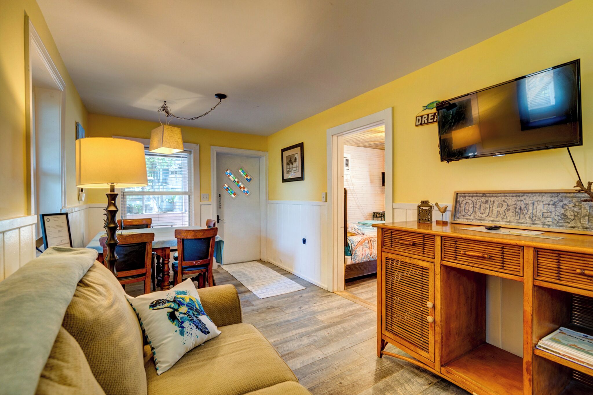 A cozy living room with a sofa, a wooden sideboard, a television, and a dining area with chairs and a table.