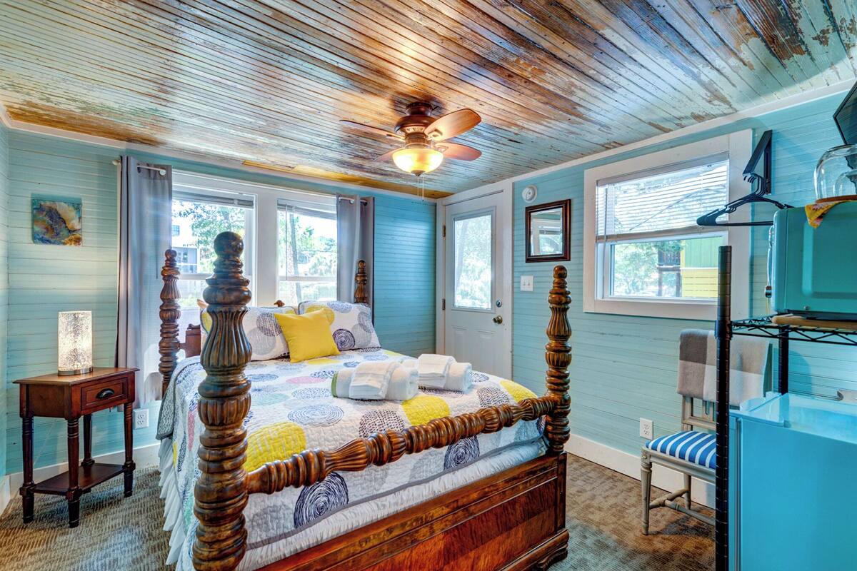 A bedroom with a wooden four-poster bed, a ceiling fan, and a dresser with a mirror.