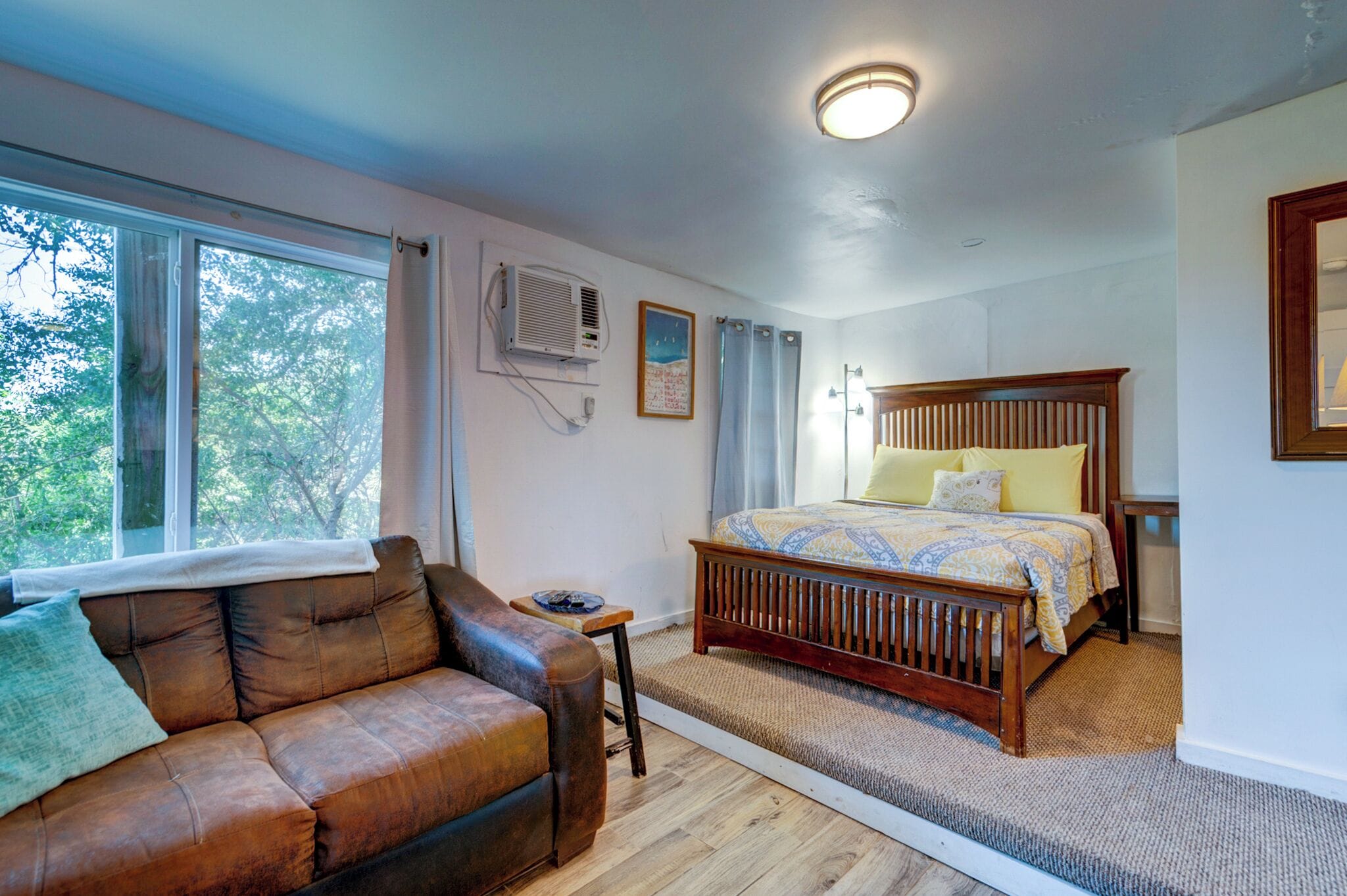 A bedroom with a wooden bed, a leather sofa, and a large window.