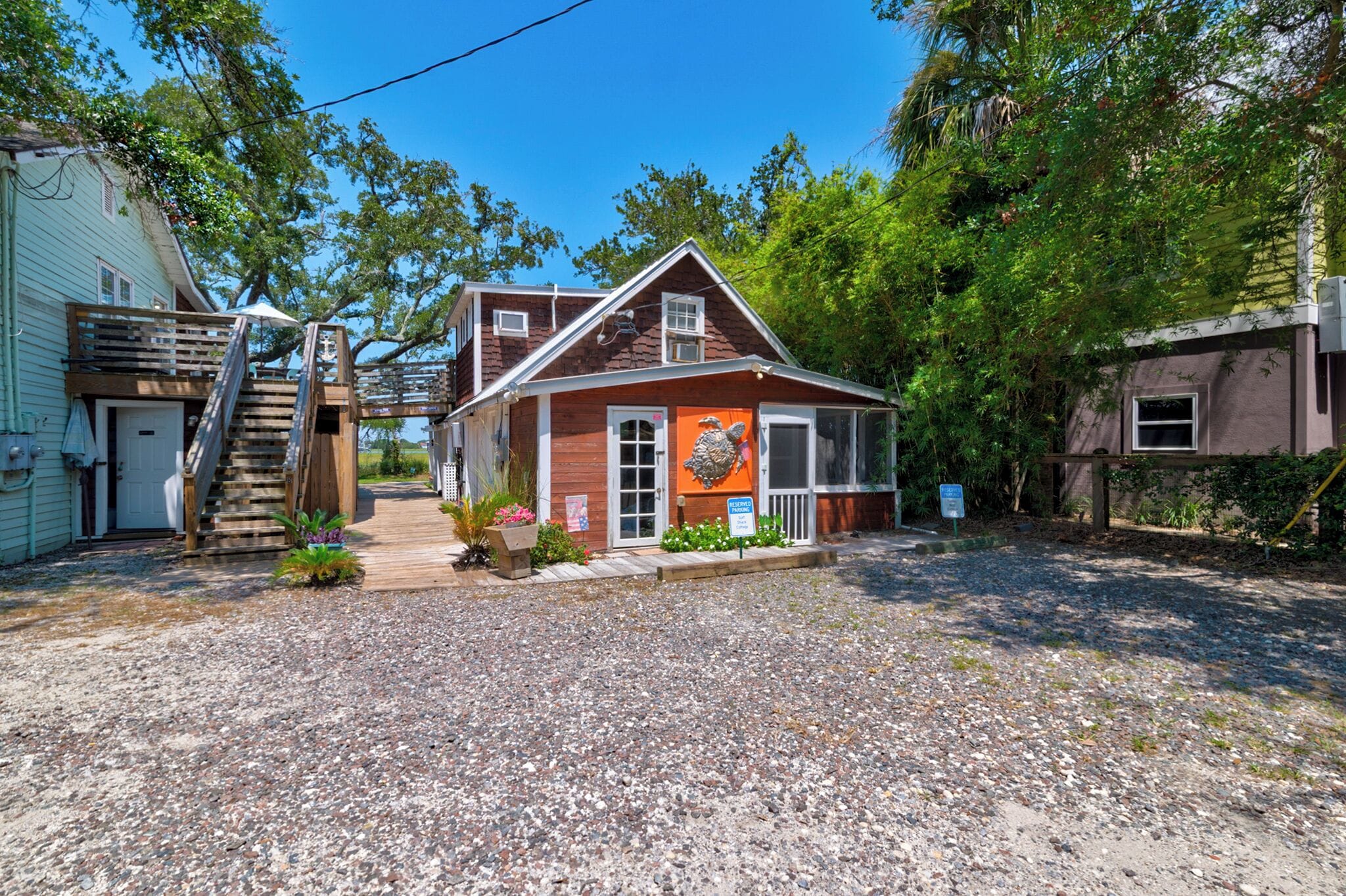 A rustic building with a wooden staircase leading to a porch, surrounded by gravel and greenery.