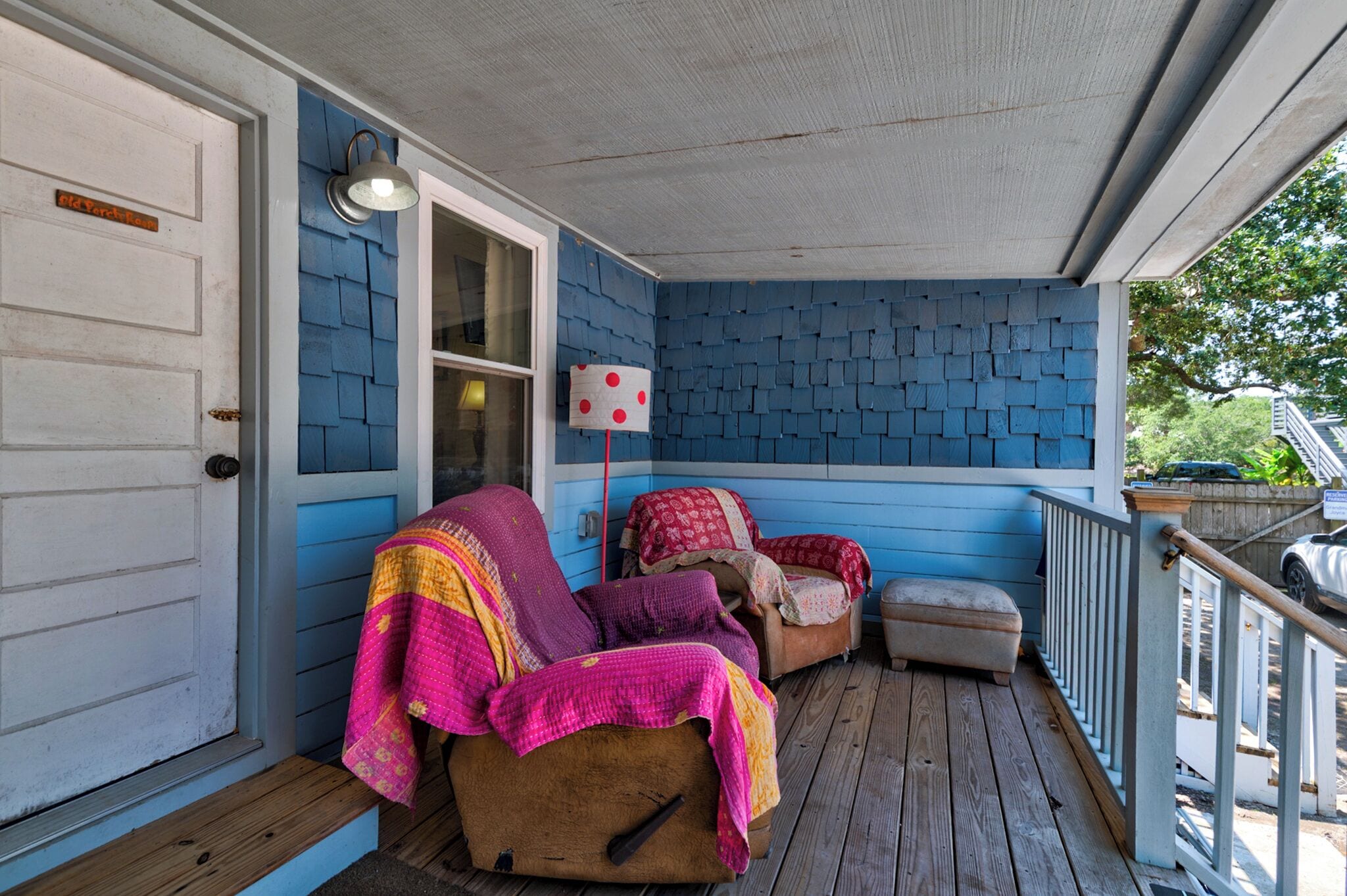 A porch with a blue exterior, a wooden bench, and a covered seating area with cushions.