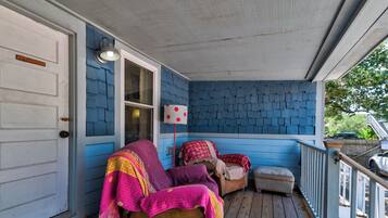 A porch with a blue exterior, a wooden bench, and a covered seating area with cushions.