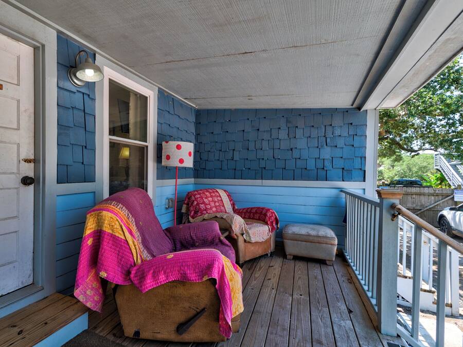 A porch with a blue exterior, a wooden bench, and a covered seating area with cushions.